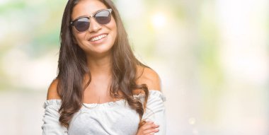 Genç güzel Arap kadın üzerinde güneş gözlüğü takıyor mutlu yüz ile gülümseyerek kameraya seyir silah geçti arka plan izole. Olumlu bir kişi.