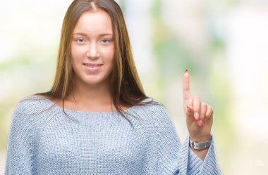 Ve parmak gülümseyen süre bir numara ile kendinden emin ve mutlu yukarıyı gösteren izole arka plan üzerinde kış kazak giyen genç güzel beyaz kadın.