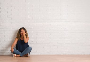 Orta yaş İspanyol kadın el yüz ve sürpriz duygu kendinden emin gülümseme ile tek gözüyle kapsayan beyaz tuğla duvarın üzerinden katta oturan.