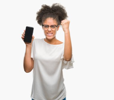 Genç güzel afro Amerikan gösteren smartphone ekran üzerinde izole arka plan ile öfke, çılgın ve yükseltilmiş eliyle diye bağıran rahatsız ve hayal kırıklığına uğramış öfke kavramı bağırarak
