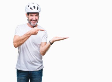 Hayret ve el ile sunulması ve parmak ile işaret ederken kameraya gülümseyen Bisiklet Emanet helment izole arka plan giyen orta yaş üst düzey ağarmış bisikletçi adam.