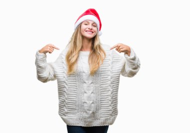 Yüzünde gülümseme ile kendinden emin görünüyorsun, kendini gururlu ve mutlu parmakları ile işaret izole arka plan üzerinde Noel şapka giyen genç güzel sarışın kadın.