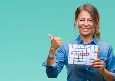 Adet takvim işaret ve başparmak kadar mutlu yüz gülümseyen tarafı ile gösteren izole arka plan üzerinde tutan orta yaş üst düzey İspanyol kadın