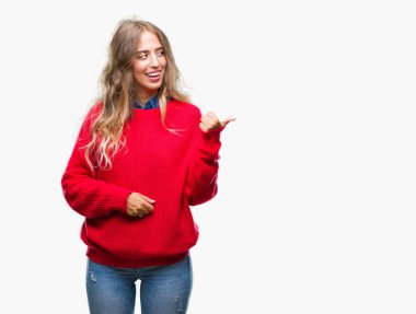 Seyir ve başparmak yanında yukarıyı mutlu yüz ile gülümseyen izole arka plan üzerinde kış kazak giyen güzel genç sarışın kadın.