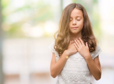 Esmer Latin kız göğüs kapalı gözlerle ellerinde ve yüzünde minnettar jest ile gülümseyen. Sağlık kavramı.