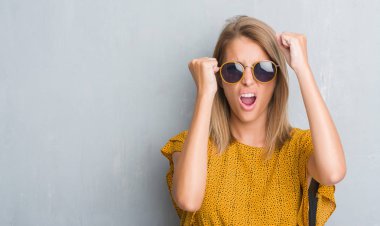 Grunge gri üzerinde duran güzel genç kadın duvar giyen retro güneş gözlüğü rahatsız ve hayal kırıklığına uğramış bağırarak öfkeyle, çılgın ve bağrışmalar yükseltilmiş el, öfke kavramı ile