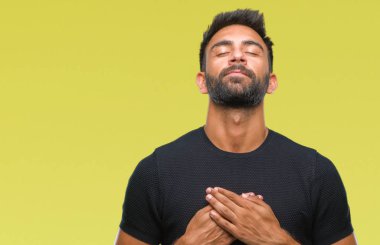 Göğüs kapalı gözler ve yüzünde minnettar jest ile yetişkin İspanyol adam ile gülümseyen izole arka plan üzerinde eller. Sağlık kavramı.