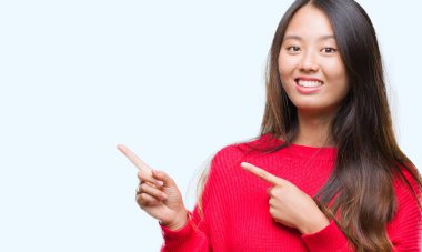 Gülümseyen ve iki elleri ve parmakları ile tarafına işaret kamera bakarak izole arka plan üzerinde kış kazak giyen genç Asyalı kadın.