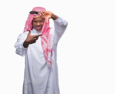 Geleneksel keffiyeh elle yapma çerçeve ve parmakları ile mutlu yüz gülümseyen izole arka plan üzerinde giyen genç Arapça Afrika adam. Yaratıcılık ve Fotoğrafçılık kavramı.