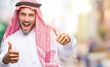 Keffiyeh el ile pozitif jest yapıyor onaylama izole arka plan üzerinde giyen genç yakışıklı adam başparmak gülümseyen ve başarı için mutlu. Kamera, kazanan jest arıyorsunuz.