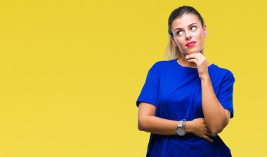 Çene düşünme hakkında soru, dalgın ifade üzerine el ile izole arka plan üzerinde rahat mavi t-shirt giyen genç güzel kadın. Düşünceli yüzüyle gülümsüyor. Şüphe kavramı.