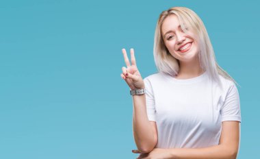 Genç Sarışın kadın mutlu yüz zafer işareti yaparken kameraya göz kırpıyor ile gülümseyen izole arka plan yüzünden. İki numaralı.