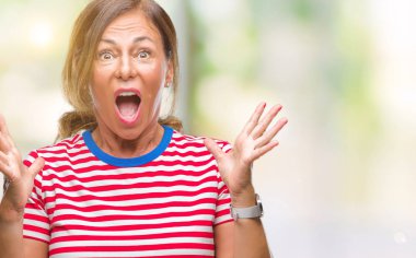 Orta yaş üst düzey İspanyol kadın deli kutluyor arka plan izole ve başarı için kaldırdı kollarını açarak hayrete ve heyecanlı çığlık gözleri açık. Kazanan kavramı