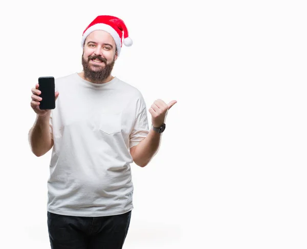 指していると幸せそうな顔を笑顔で側まで親指で示す分離の背景にクリスマス帽子 表示中のスマート フォンの画面を着た若い白人男 — ストック写真