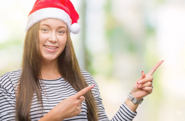 笑顔で側に つの手と指で指しているカメラを見て孤立の背景にクリスマスの帽子をかぶって若い美しい白人女性 — ストック写真