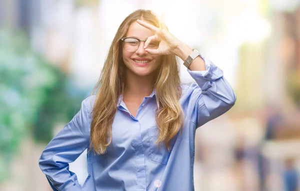 Young beautiful blonde business woman wearing glasses over isolated background doing ok gesture with hand smiling, eye looking through fingers with happy face.
