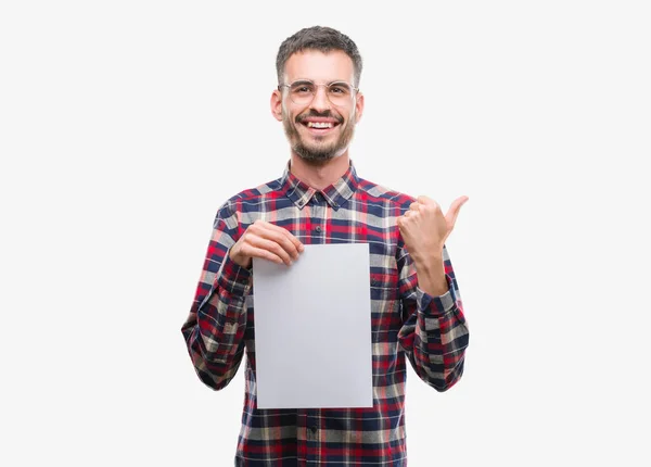 年轻的时髦的成人男子拿着空白的纸页指向和显示与拇指面带笑脸微笑 — 图库照片
