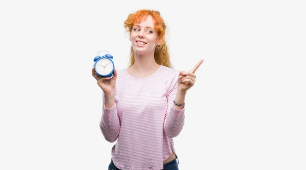 Jovem Ruiva Segurando Despertador Muito Feliz Apontando Com Mão Dedo — Fotografia de Stock