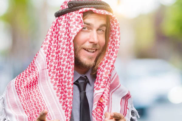 年轻英俊的阿拉伯男子与长头发戴 Keffiyeh 在孤立的背景指向相机与快乐和滑稽的脸 良好的能量和共鸣 — 图库照片
