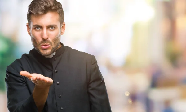 Young catholic christian priest man over isolated background looking at the camera blowing a kiss with hand on air being lovely and sexy. Love expression.