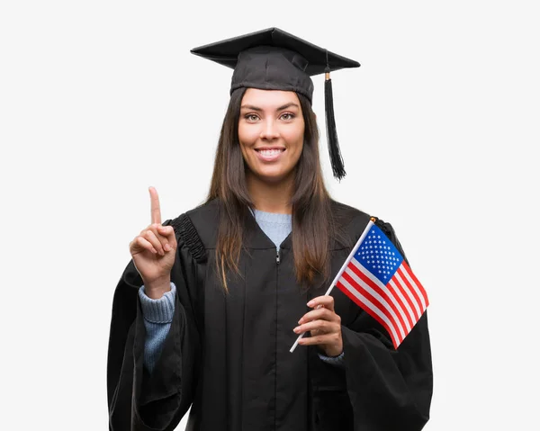 Mujer Hispana Joven Vistiendo Uniforme Graduado Sosteniendo Bandera América Sorprendida —  Fotos de Stock