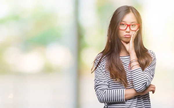 年轻的亚洲妇女戴着眼镜在孤立的背景下思维疲惫和厌倦与交叉手臂的抑郁症问题 — 图库照片