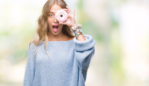 Beautiful young blonde woman eating pink donut over isolated background scared in shock with a surprise face, afraid and excited with fear expression
