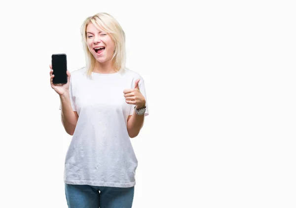 年轻美丽的金发女人在孤独的背景下展示着智能手机的屏幕 开心地笑着做着好的手势 用手指竖起大拇指 很好的标志 — 图库照片