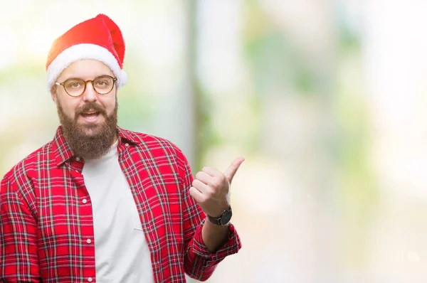 若い白人男が探していると親指側に上向きの幸せそうな顔を浮かべて隔離された背景にクリスマスの帽子をかぶって — ストック写真