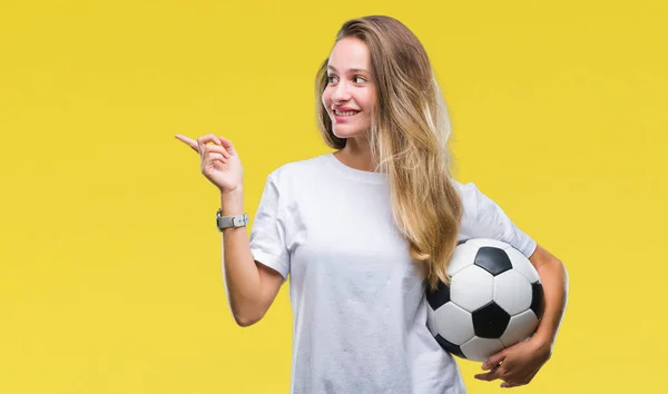 若い美しいブロンドの女性側の手と指で指す非常に幸せの孤立した背景にサッカー ボールを保持しています — ストック写真