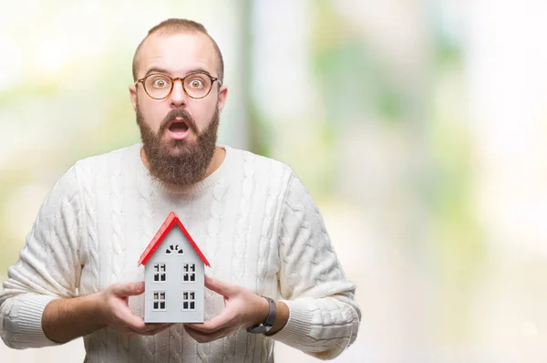 Young caucasian real state agent man holding house isolated background scared in shock with a surprise face, afraid and excited with fear expression