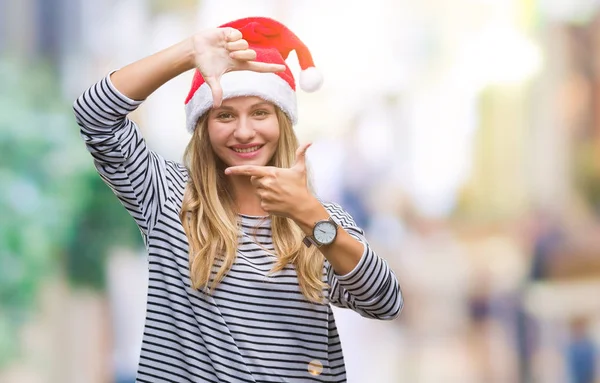 年轻美丽的金发女子戴着圣诞节帽子在孤立的背景微笑制作框架与手和手指愉快的脸 创意与摄影理念 — 图库照片