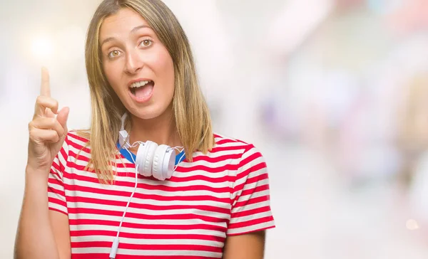 年轻美丽的女人听音乐戴着耳机在孤立的背景下 指着成功的想法 退出和快乐 第一个 — 图库照片