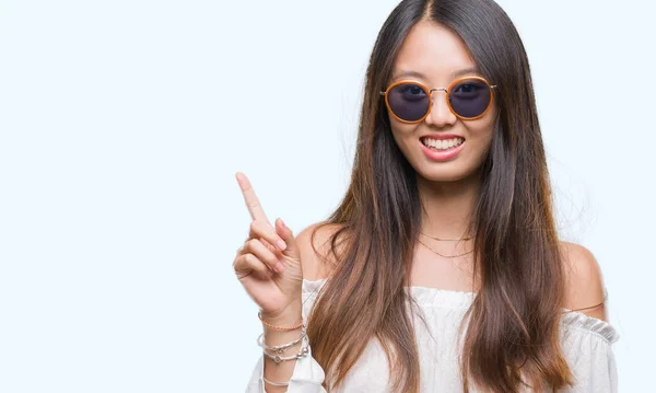 Jonge Aziatische Vrouw Zonnebril Dragen Geïsoleerde Achtergrond Wijzende Vinger Omhoog — Stockfoto