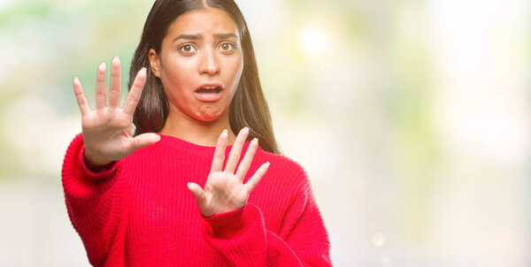 Young beautiful arab woman wearing winter sweater over isolated background afraid and terrified with fear expression stop gesture with hands, shouting in shock. Panic concept.