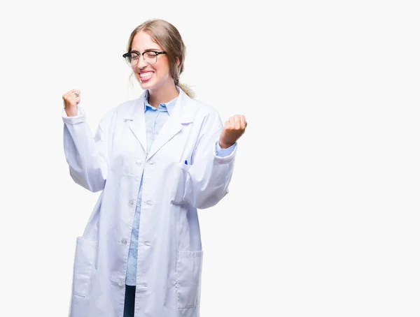 美丽的年轻金发碧眼的医生妇女穿着白色外套在孤立的背景非常高兴和兴奋做优胜者手势与胳膊举起 微笑和尖叫为成功 庆祝理念 — 图库照片