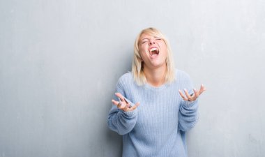 Grunge yetişkin beyaz kadın kış kazak deli giyen duvar gri ve deli bağırarak ve agresif ifade ve silah kaldırdı bağırıyor. Hayal kırıklığı kavramı.