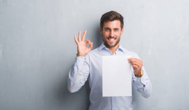 Boş kağıt sayfası sözleşme parmak, mükemmel sembolü ile ok işareti yapıyor tutan gri grunge duvarın üzerinden yakışıklı genç