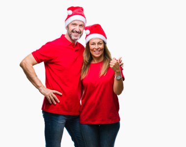 Orta yaş İspanyol çift arıyorum ve başparmak yanında yukarıyı mutlu yüz ile gülümseyen izole arka plan üzerinde Noel şapka.