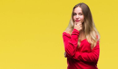 Emin çapraz kollar ve çeneme kaldırdı el ile gülümseme ile kameraya bakarak izole arka plan üzerinde kırmızı kazaklı giyen genç güzel sarışın kadın. Pozitif düşünce.