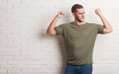 Kol kasları gururlu gülümseyen gösterilen beyaz tuğla duvardan ayakta beyaz delikanlı. Fitness kavramı.