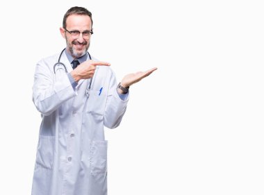 Hayret ve el ile sunulması ve parmak ile işaret ederken kameraya gülümseyen Tıbbi üniforma izole geçmişi giyen orta yaş üst düzey ağarmış Doktor adam.