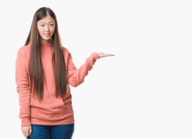 Arka plan neşeli sunulması ve kameraya bakarak avucunun ile işaret gülümseyen spor sweathshirt giyen genç Çinli kadın izole.