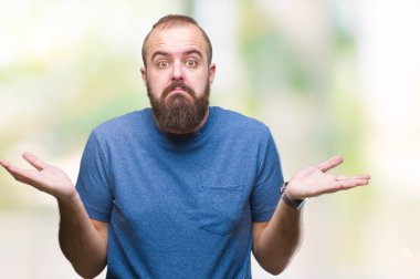 Genç beyaz hipster adam izole arka plan clueless ve şaşkın bir ifadeyle kollar ve eller kaldırdı. Şüphe kavramı.