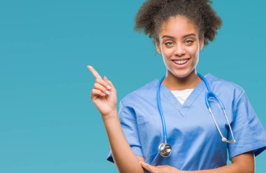 Kameraya bakarak yan el ve parmak ile işaret eden genç afro Amerikalı doktor kadın yüzünde kocaman bir gülümseme ile izole arka plan üzerinde.