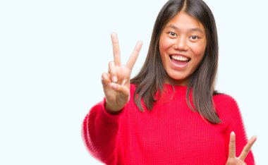 Genç Asyalı kadın parmaklarını zafer işareti yaparken gösterilen kamera seyir gülümseyen izole arka plan üzerinde kış kazak giyiyor. İki numaralı.