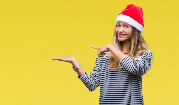 年轻美丽的金发女子戴着圣诞节帽子在孤立的背景惊讶和微笑的相机 而用手和手指指着 — 图库照片