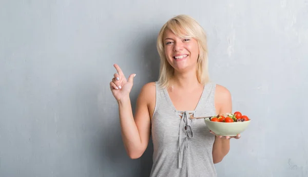 成年白种人女人在垃圾灰墙吃西红柿沙拉很高兴地指着手和手指到一边 — 图库照片