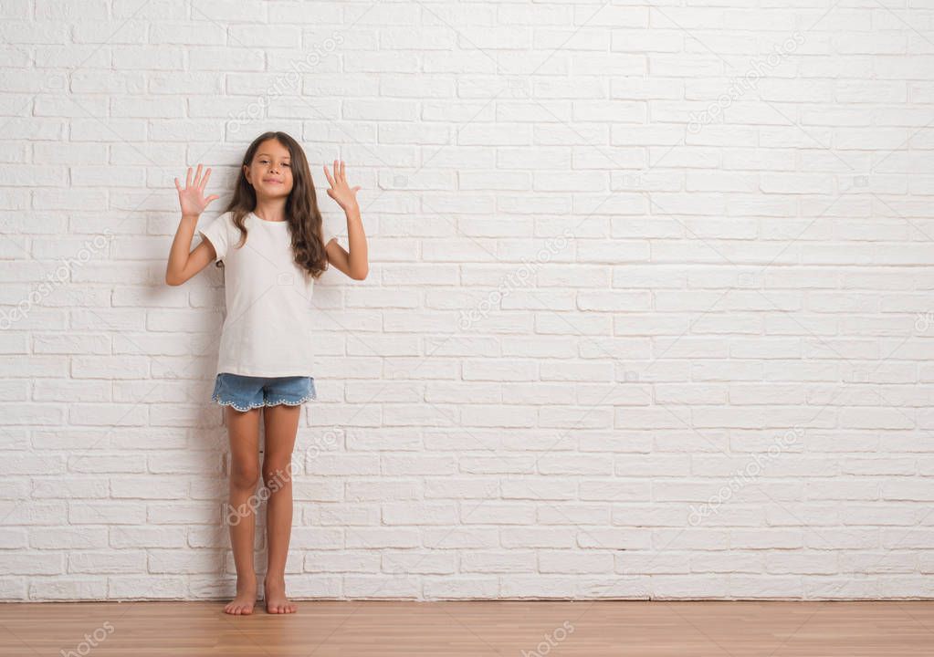 Young hispanic kid stading over white brick wall showing and pointing up with fingers number nine while smiling confident and happy.