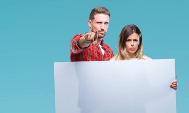 Genç çift kamera ve size parmak ile işaret izole arka plan üzerinde boş afiş tutarak birlikte, el işareti, pozitif ve kendinden emin bir jest ön